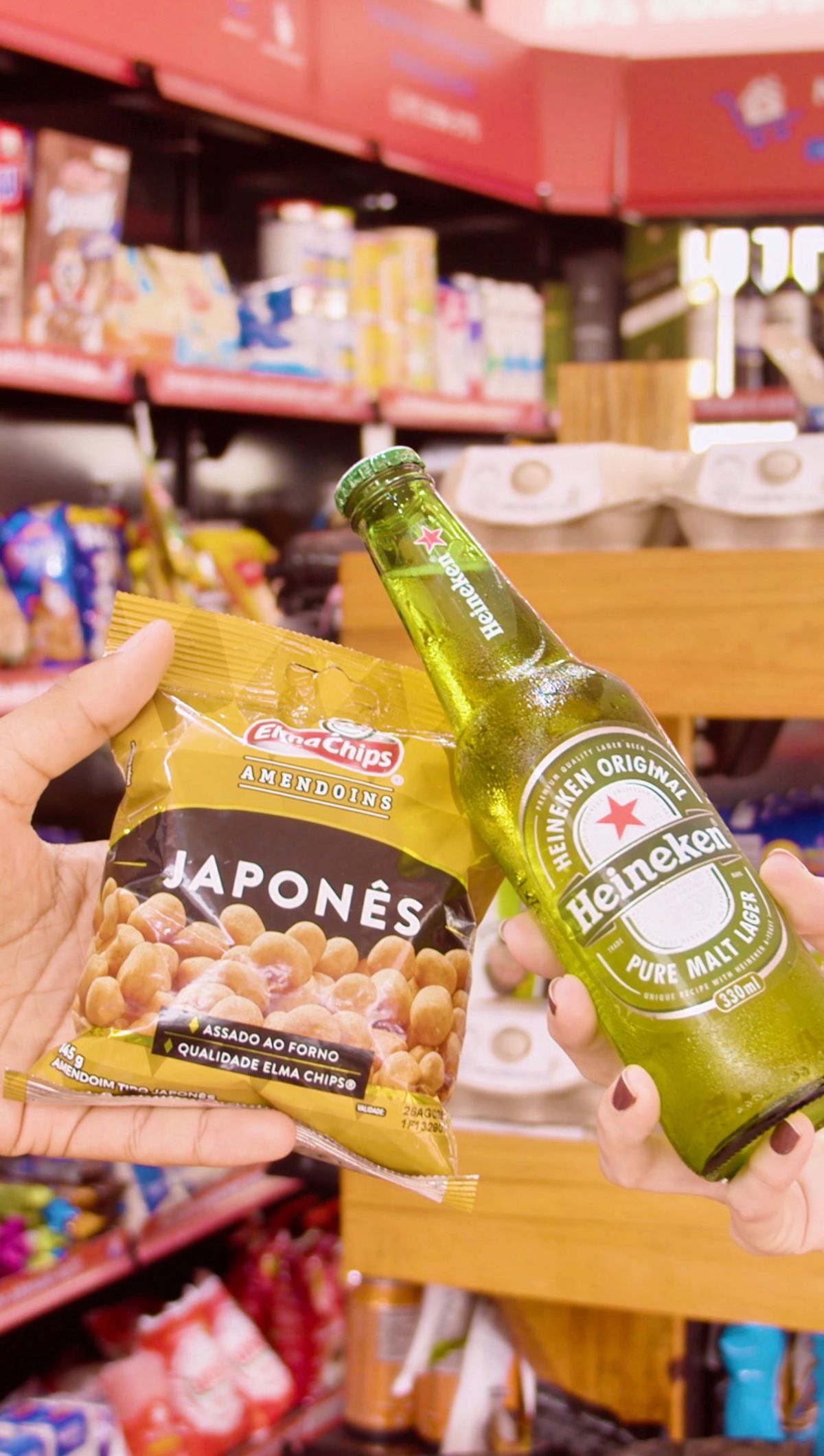 Amendoim japonês e cerveja segurados em frente à gôndola