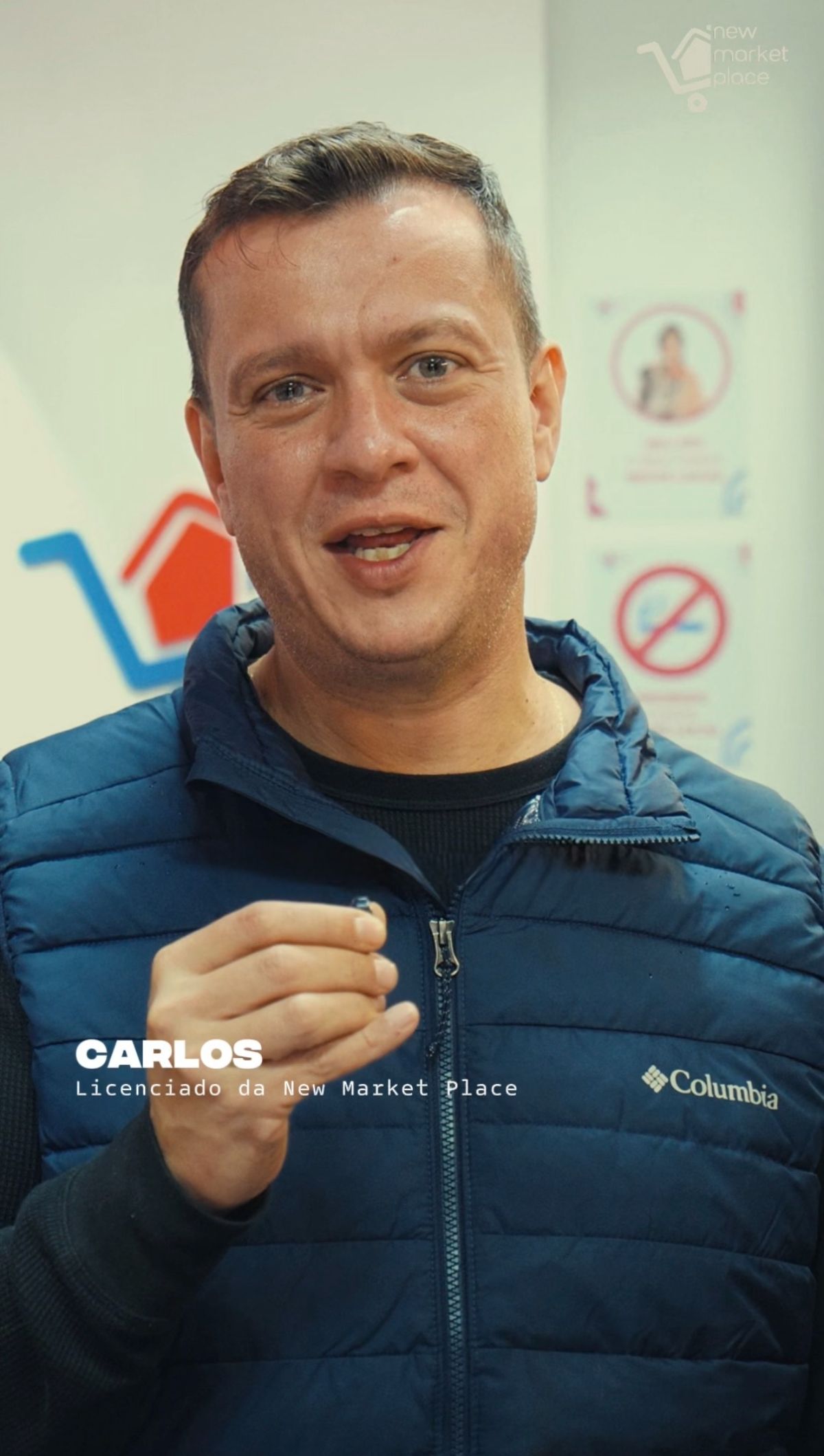 Carlos, licenciado da New Market Place, fala em frente ao logotipo da loja