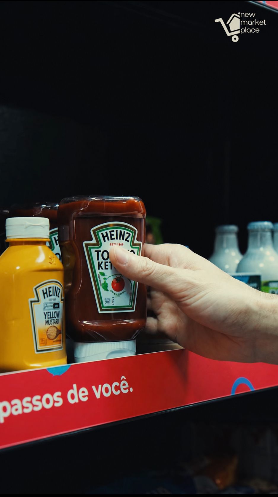 Mão pega um ketchup na prateleira, ao lado da mostarda e de garrafas de leite